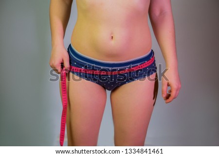 A girl with overweight measures the size of the ass with a tape. Female body on a gray background