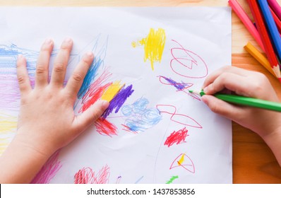 Girl Painting On Paper Sheet With Colour Pencils On The Wooden Table At Home / Child Kid Doing Drawing Picture And Colorful Crayon