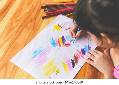 Girl Painting On Paper Sheet With Colour Pencils On The Wooden Table At Home / Child Kid Doing Drawing Picture And Colorful Crayon