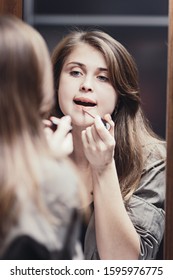 girl paints her lips with lipstick in front of a mirror at home, a young woman doing makeup, a concept of female natural beauty and cosmetics