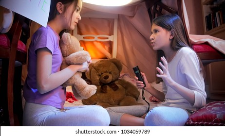 Girl In Pajamas Telling Scary Story To Her Friend In Selfmade Tent At Bedroom