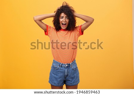 Girl panicking not being ready meet boyfriend parents. Portrait of shocked troubled and concerned gloomy girlfriend with afro hairstyle holding hands on hair yelling from shock over orange background