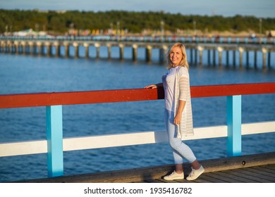 a girl in pants and a jacket stands on a pier near the Baltic Sea.Palanga
