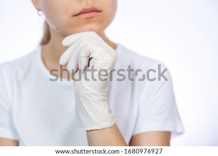 Girl paramedic puts on white medical gloves on hands. Protection against germs and viruses. She is in a white T-shirt on a white background.