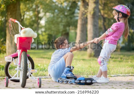 girl in park, helps boy with roller skates to stand up 