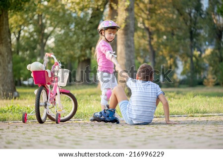 girl in park, helps boy with roller skates to stand up