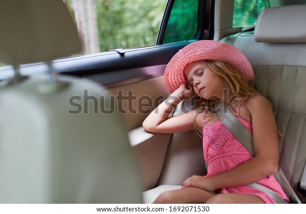 Girl peacefully sleeps on back seat in\
the car on the journey into summer\
vacation