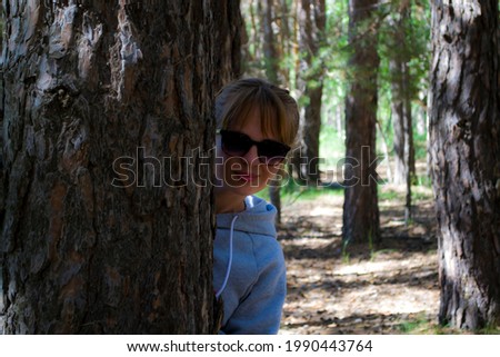 A girl peeks out from behind a tree in the sun with goggles. Walk in the park in the open air.