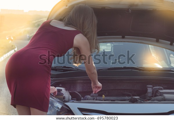 The girl\
peeks under the hood of the car. Young woman near broken car needs\
assistance. looking under opened\
hood.