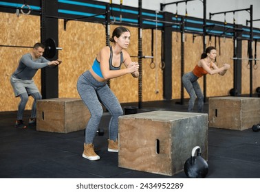 Girl performs exercises handstand push-ups, squats, hill climbing, kettlebell squats using fitness platform, cube. Female gym visitor performs series of repetitions movements with sport equipment - Powered by Shutterstock