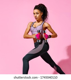 Girl performs exercises using dumbbells. Photo of african american girl in black sportswear on pink background. Strength and motivation