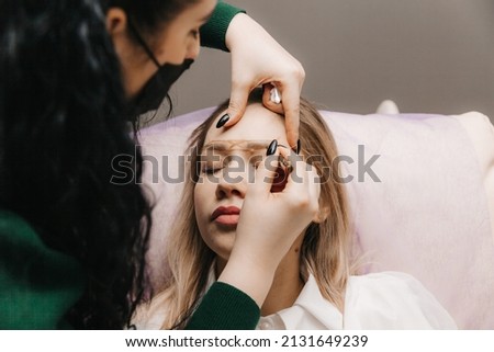 girl with permanent makeup on her eyebrows. The makeup artist makes markings with a brown pencil for eyebrow tattooing.