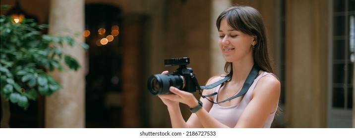 Girl photographer with a camera at work on the set in the studio room. Young beautiful woman - a professional photographer with a camera and a flash takes pictures in a studio with natural light - Powered by Shutterstock