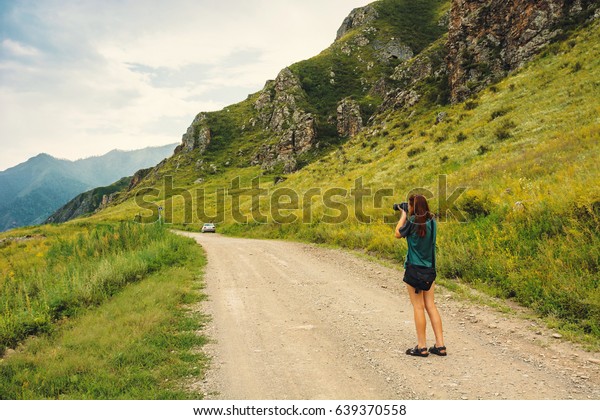 Girl photographs on\
the camera being on the mountain road. The model is turned with the\
back. Mountain Altai.