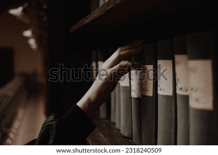 A girl picking an antique book on a shelf of a reading hall in a library with her pale hand. Concept of literature, reading, literacy, and knowledge.