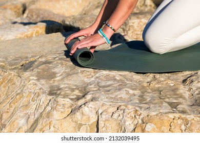 Girl Picking Up Yoga Mat On Beach Rocks
