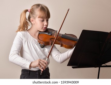 Girl with pigtails playing the violin looking at the score on a music stand. Horizontal composition. Front view. - Powered by Shutterstock