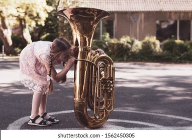 A girl with pigtails tries to play tuba - Shutterstock ID 1562450305