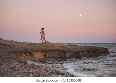 Girl in pink dress at the ocean at sunset 