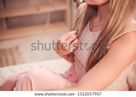 A girl in a pink dress touches the ends of her hair