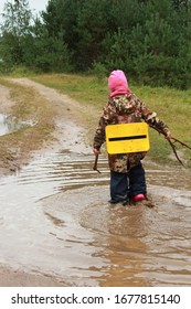 A Girl In A Pink Hat, Boots, A Waterproof Jacket And Waterproof Trousers Conquers A Summer Puddle