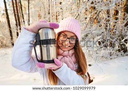 girl in a pink hat with a thermos in the winter in the forest