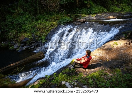 Girl in a pink jacket sits and admires unique, beautiful waterfall on Canungra Creek Circuit trail, Lamington National Park (O'Reilly's), Gold Coast, Queensland, Australia	