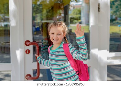 A Girl With A Pink Satchel Opens The School Door. Children Go Out To Study After Vacation And The Coronavirus Epidemic. The New School Year