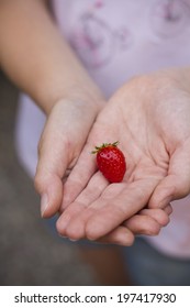 Girl with pink shirt showing a strawberry resting on her hands