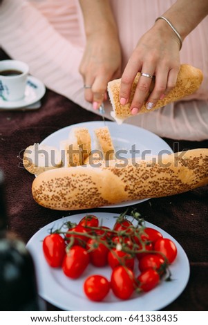 Girl in pink skirt cut baguette on a plate next to cherry tomatoes, white cup of coffee and a basket.