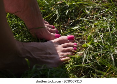 A Girl With Pink Toenails Stands Barefoot On The Green Grass