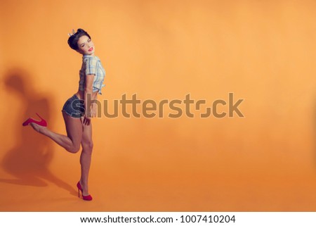 girl in pin-up style on a yellow background flexes leg