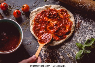 Girl is placing tomato sauce on fresh pizza