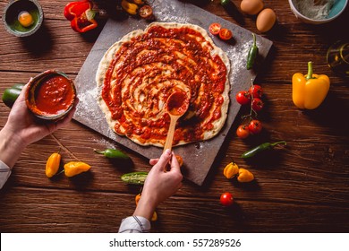 Girl is placing tomato sauce on fresh pizza