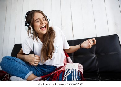 Girl in plaid listening music in headphones, sitting on sofa.