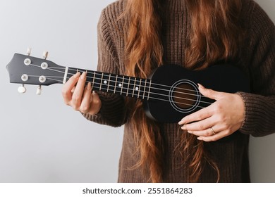 Girl playing a black ukulele. Holding a chord on the fretboard with her hand. Four string guitar. Black wooden musical instrument in focus. Artistic background of a musician. Lesson how to play. - Powered by Shutterstock