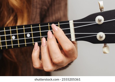 Girl playing a black ukulele. Holding a chord on the fretboard with her hand. Four string guitar. Black wooden musical instrument in focus. Artistic background of a musician. Lesson how to play. - Powered by Shutterstock