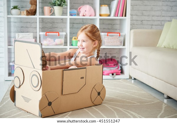 Girl playing with\
car made of cardboard box