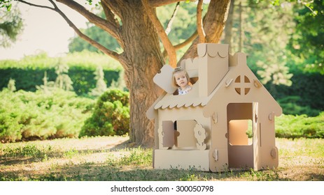 girl playing in cardboard house in a city park on a sunny day