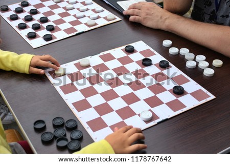 Girl playing checkers outdoor. Checkers game board on wooden table with black and white checkers