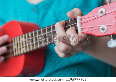 Girl playing chord on red soprano ukulele