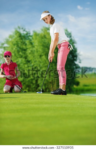Girl playing\
golf and hitting by putter on\
green