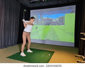 Girl playing golf on screen and golf simulator. Young golfer playing golf video game indoors