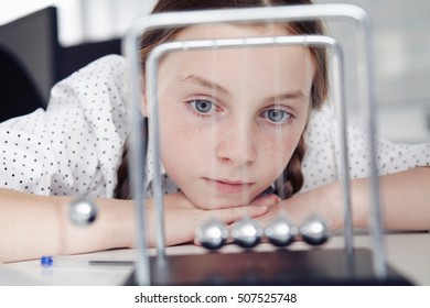 Girl Playing With Newton's Cradle On Desk