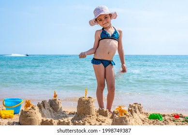 Girl playing on a sandy beach on summer vacation. A child is building a sand castle on the sea. 
