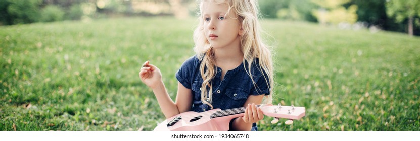 Girl Playing Pink Guitar Toy Outdoors. Child Playing Music And Singing Song In Park. Music Hobby Activity For Children Kids.Real Authentic Candid Childhood Moment. Web Banner Header.