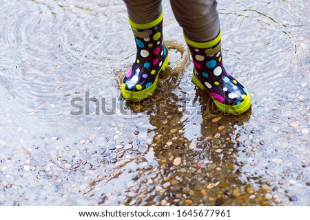 Girl Playing in rain puddles on a urban floor with colorful spotted boots