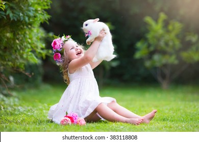 Girl Playing With Real Rabbit In Sunny Garden. Child And Bunny On Easter Egg Hunt In Flower Meadow. Toddler Kid Feeding Pet Animal. Kids And Pets Play.  Fun And Friendship For Animals And Children.