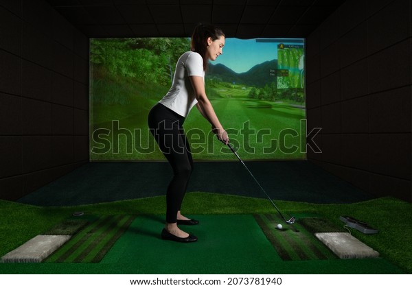 A girl playing screen\
golf, golf simulator.Young golf player having playing video-game\
golf indoors.                                                      \
           