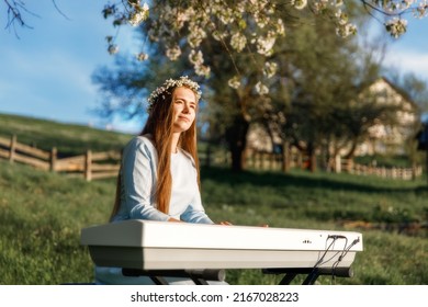 Girl playing a synthesizer piano in nature at sunset. A woman is 22 years old. An electric piano stands in a field in a village. Spring day in the countryside. 